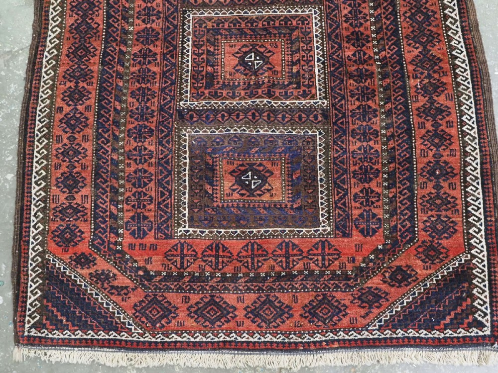 An antique Baluch hand-knotted wool rug featuring five geometric square medallions along a central field in deep red, dark navy blue, and terracotta tones. View V
