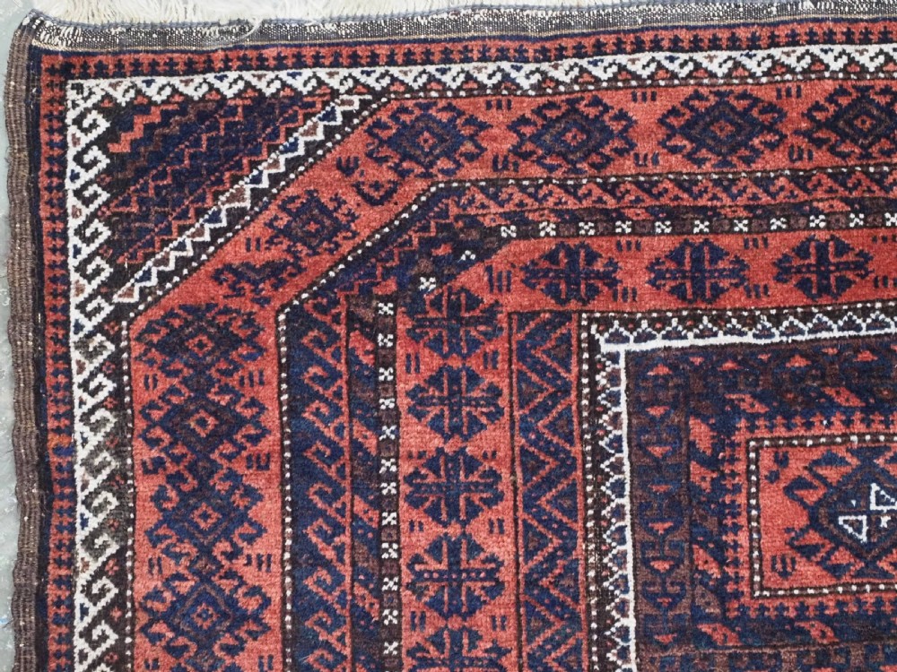 An antique Baluch hand-knotted wool rug featuring five geometric square medallions along a central field in deep red, dark navy blue, and terracotta tones. View VI