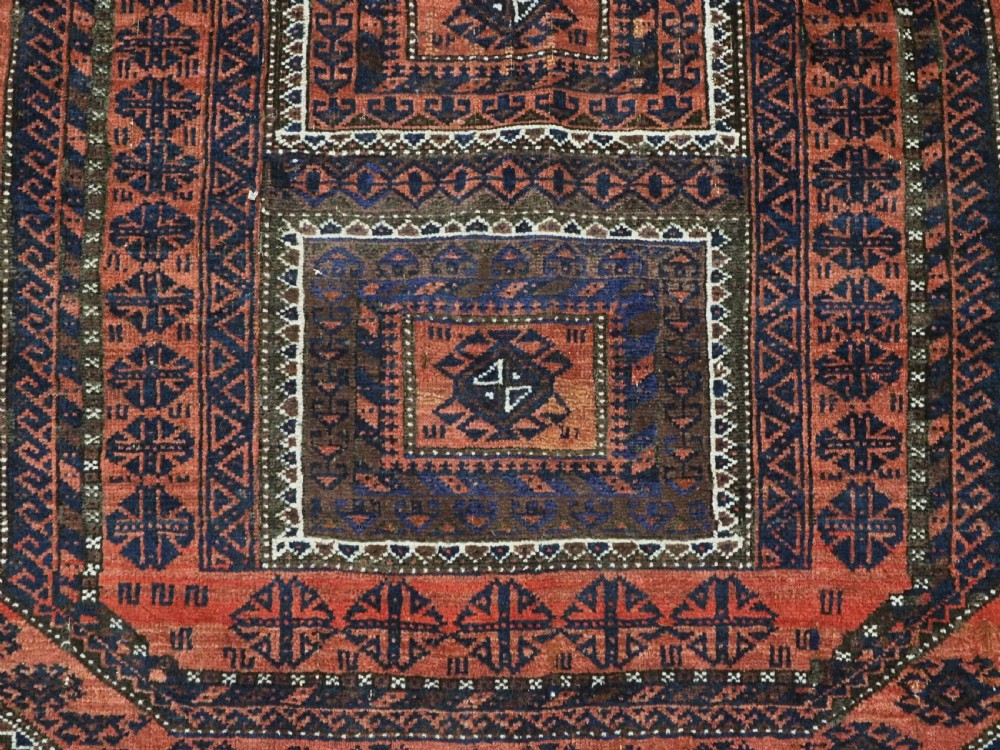 An antique Baluch hand-knotted wool rug featuring five geometric square medallions along a central field in deep red, dark navy blue, and terracotta tones. View X