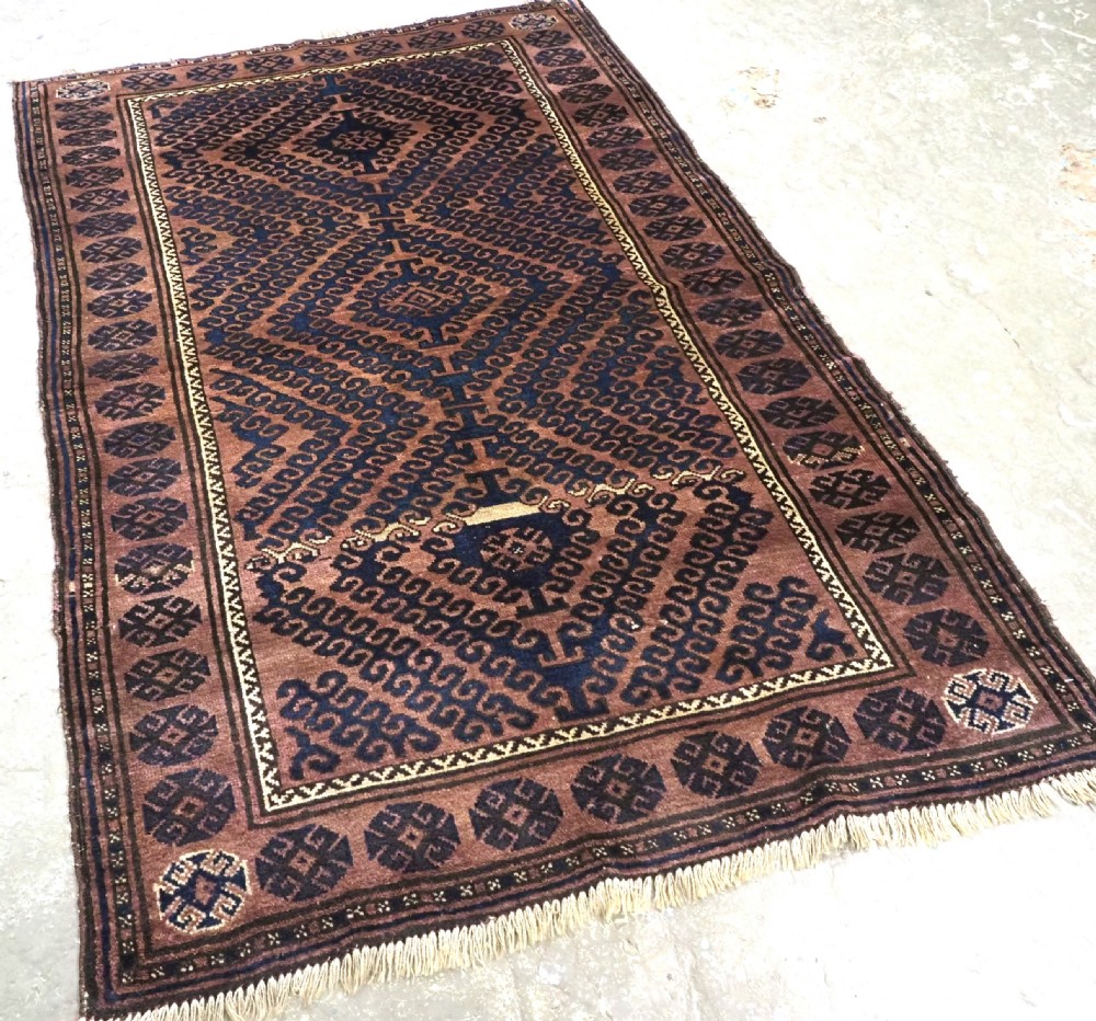 An antique hand-knotted Afghan Baluch wool rug featuring repeating geometric diamond motifs in dark brown and indigo blue tones. View II