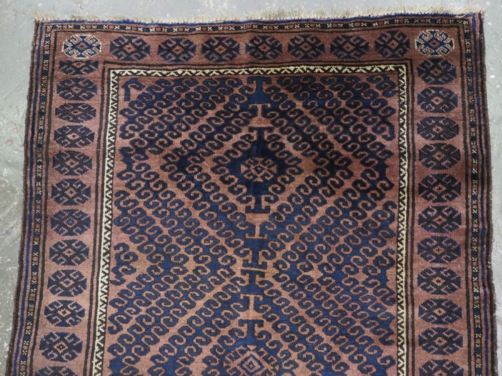 An antique hand-knotted Afghan Baluch wool rug featuring repeating geometric diamond motifs in dark brown and indigo blue tones. View III