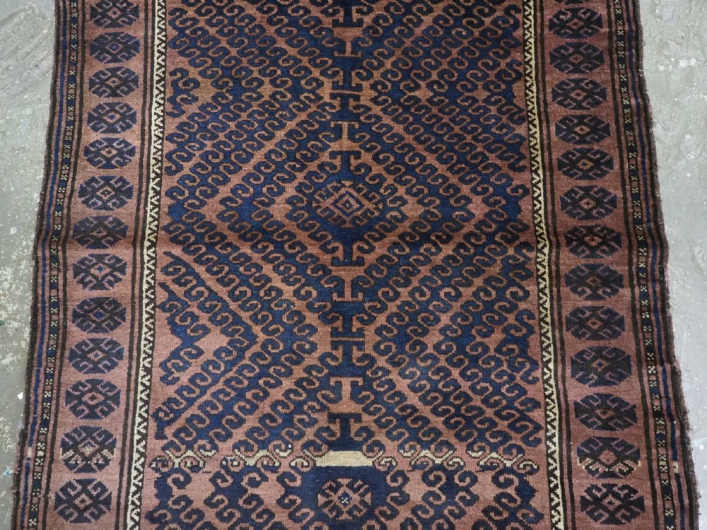 An antique hand-knotted Afghan Baluch wool rug featuring repeating geometric diamond motifs in dark brown and indigo blue tones. View IV