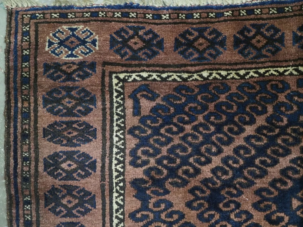 An antique hand-knotted Afghan Baluch wool rug featuring repeating geometric diamond motifs in dark brown and indigo blue tones. View V