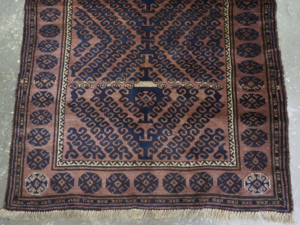 An antique hand-knotted Afghan Baluch wool rug featuring repeating geometric diamond motifs in dark brown and indigo blue tones. View VI