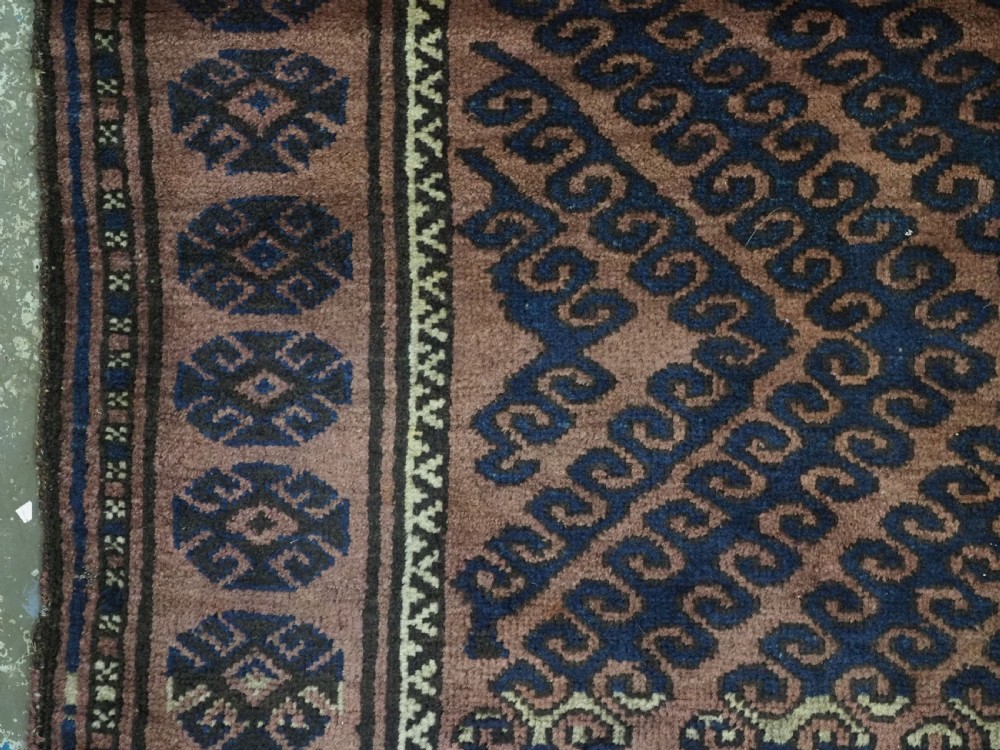 An antique hand-knotted Afghan Baluch wool rug featuring repeating geometric diamond motifs in dark brown and indigo blue tones. View VII
