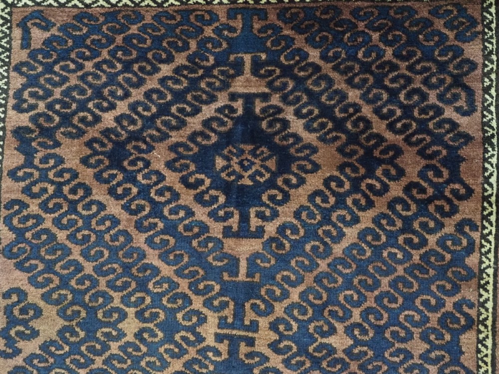 An antique hand-knotted Afghan Baluch wool rug featuring repeating geometric diamond motifs in dark brown and indigo blue tones. View VIII