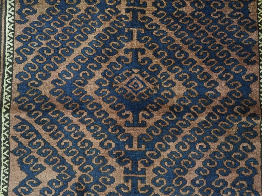 An antique hand-knotted Afghan Baluch wool rug featuring repeating geometric diamond motifs in dark brown and indigo blue tones. View IX