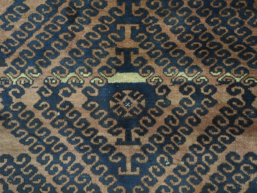 An antique hand-knotted Afghan Baluch wool rug featuring repeating geometric diamond motifs in dark brown and indigo blue tones. View X
