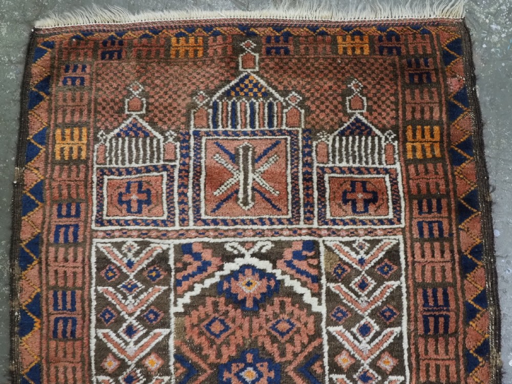 An antique hand-knotted wool prayer rug featuring a three-niche architectural design in terracotta, dark brown, and indigo blue tones with fringed edges. View III