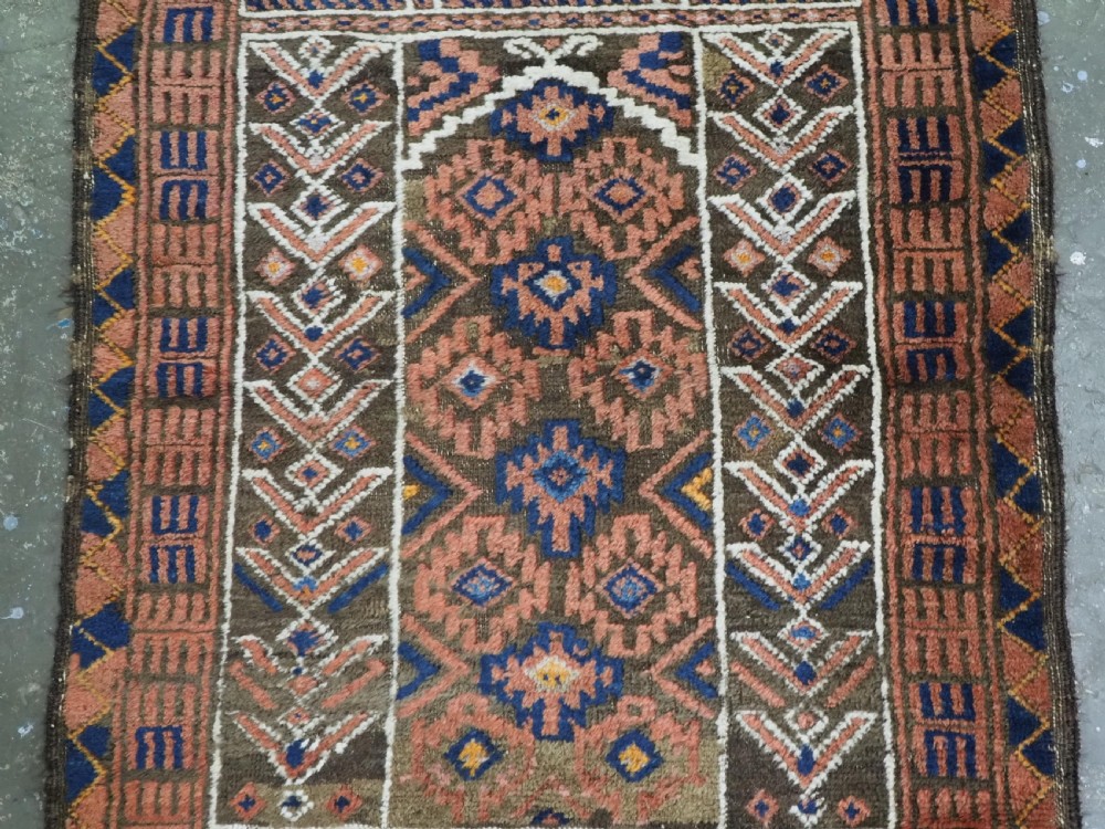 An antique hand-knotted wool prayer rug featuring a three-niche architectural design in terracotta, dark brown, and indigo blue tones with fringed edges. View IV