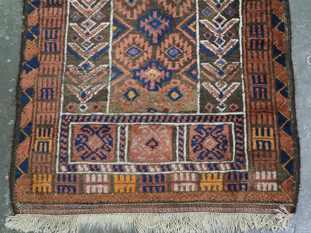 An antique hand-knotted wool prayer rug featuring a three-niche architectural design in terracotta, dark brown, and indigo blue tones with fringed edges. View V