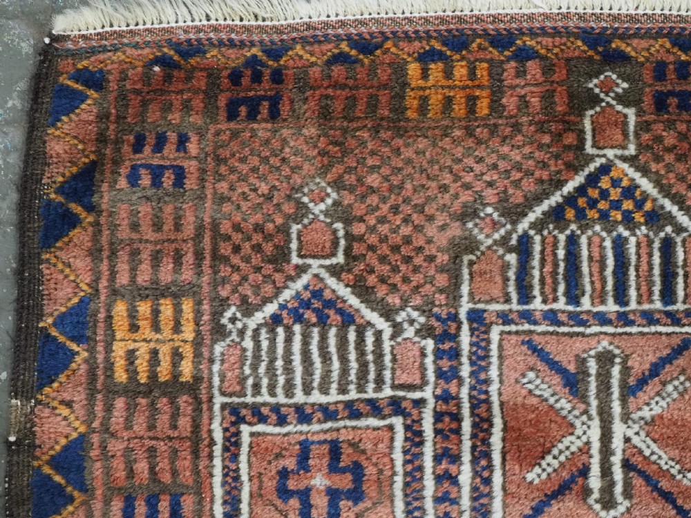An antique hand-knotted wool prayer rug featuring a three-niche architectural design in terracotta, dark brown, and indigo blue tones with fringed edges. View VI