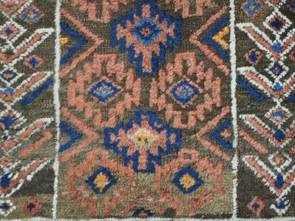 An antique hand-knotted wool prayer rug featuring a three-niche architectural design in terracotta, dark brown, and indigo blue tones with fringed edges. View X