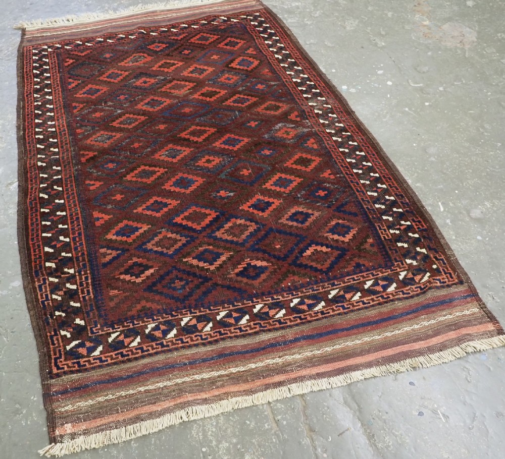 An antique hand-knotted wool rug featuring a repeating diamond lattice pattern in terracotta red and dark navy blue with geometric borders and fringed edges. View II