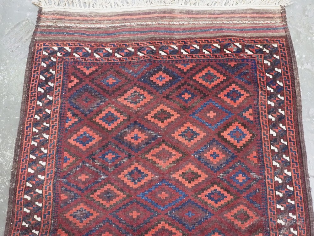 An antique hand-knotted wool rug featuring a repeating diamond lattice pattern in terracotta red and dark navy blue with geometric borders and fringed edges. View III