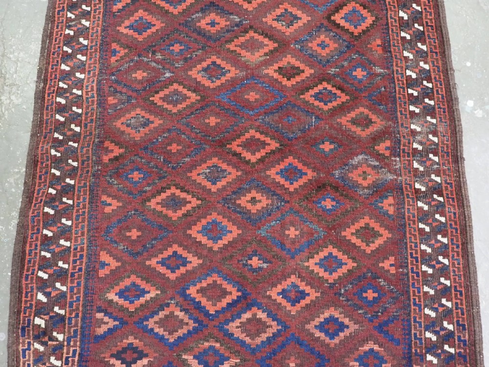 An antique hand-knotted wool rug featuring a repeating diamond lattice pattern in terracotta red and dark navy blue with geometric borders and fringed edges. View IV