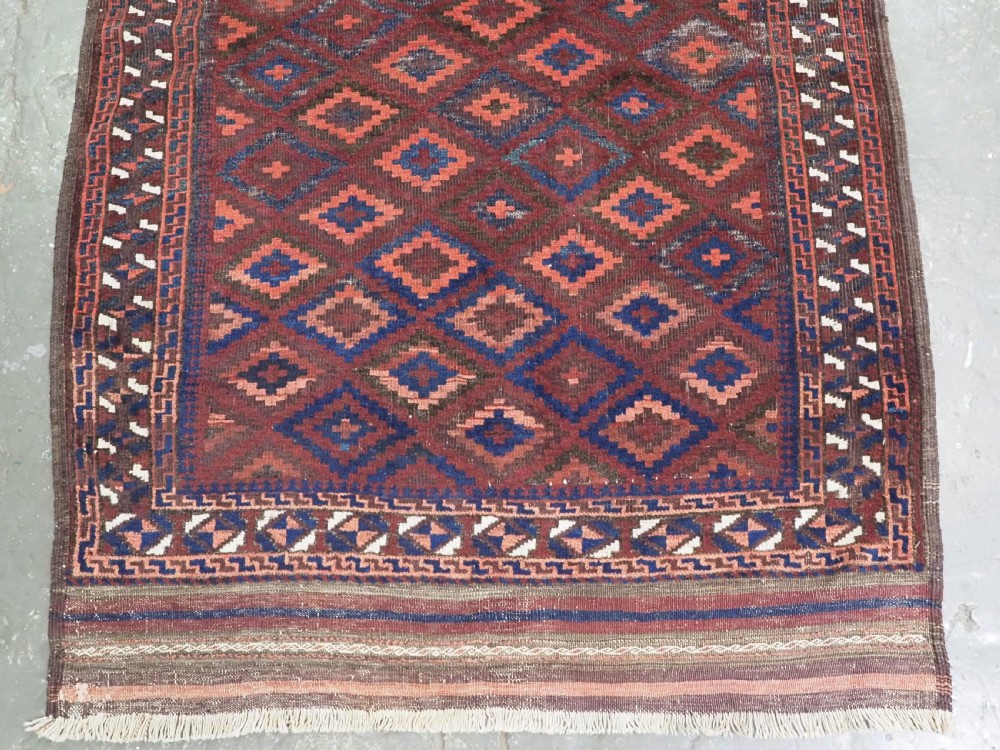 An antique hand-knotted wool rug featuring a repeating diamond lattice pattern in terracotta red and dark navy blue with geometric borders and fringed edges. View V