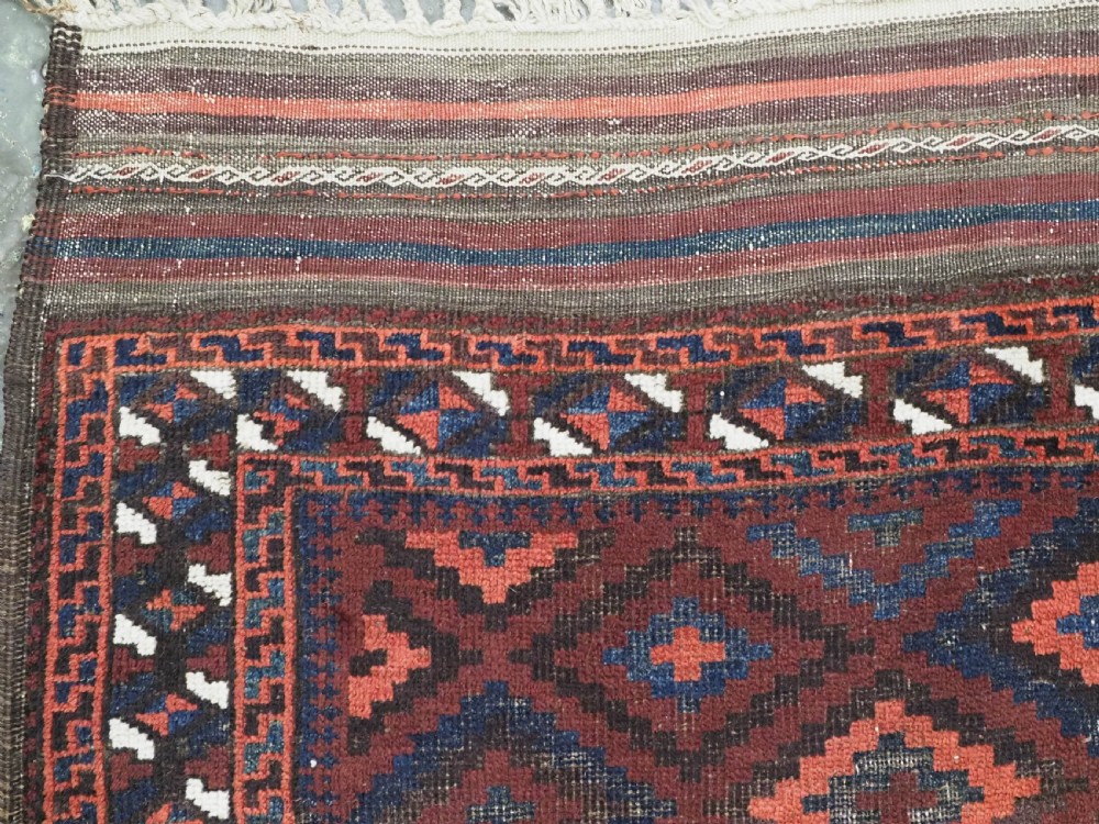 An antique hand-knotted wool rug featuring a repeating diamond lattice pattern in terracotta red and dark navy blue with geometric borders and fringed edges. View VI