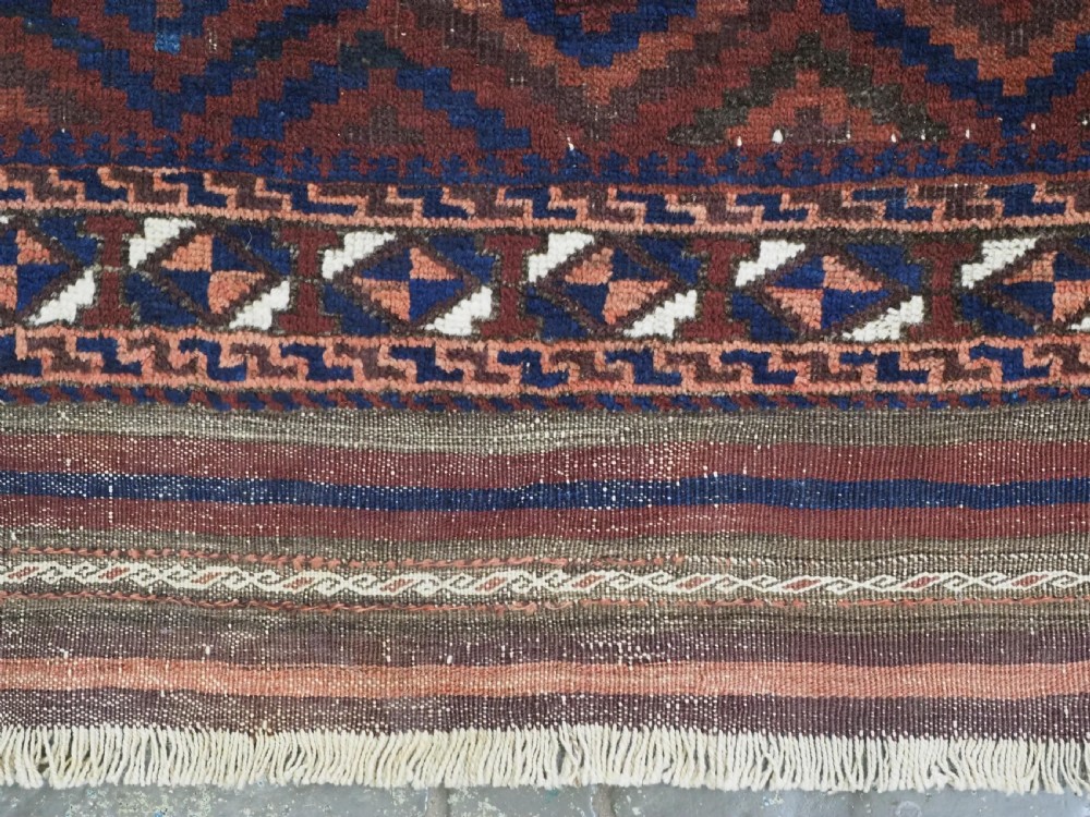 An antique hand-knotted wool rug featuring a repeating diamond lattice pattern in terracotta red and dark navy blue with geometric borders and fringed edges. View VII