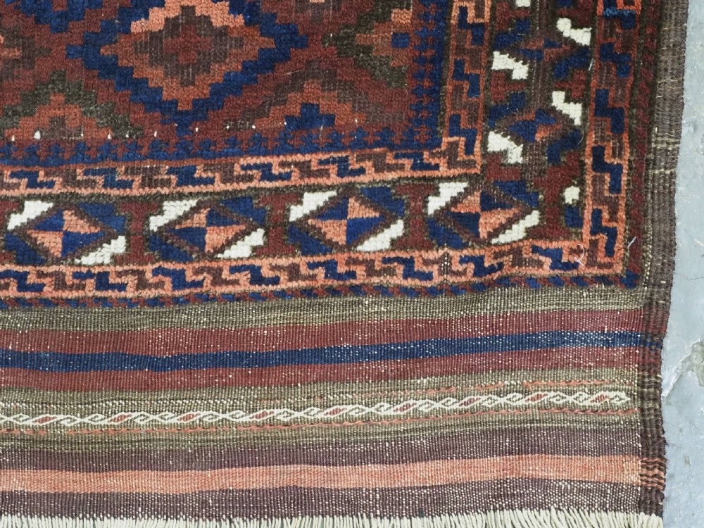 An antique hand-knotted wool rug featuring a repeating diamond lattice pattern in terracotta red and dark navy blue with geometric borders and fringed edges. View VIII