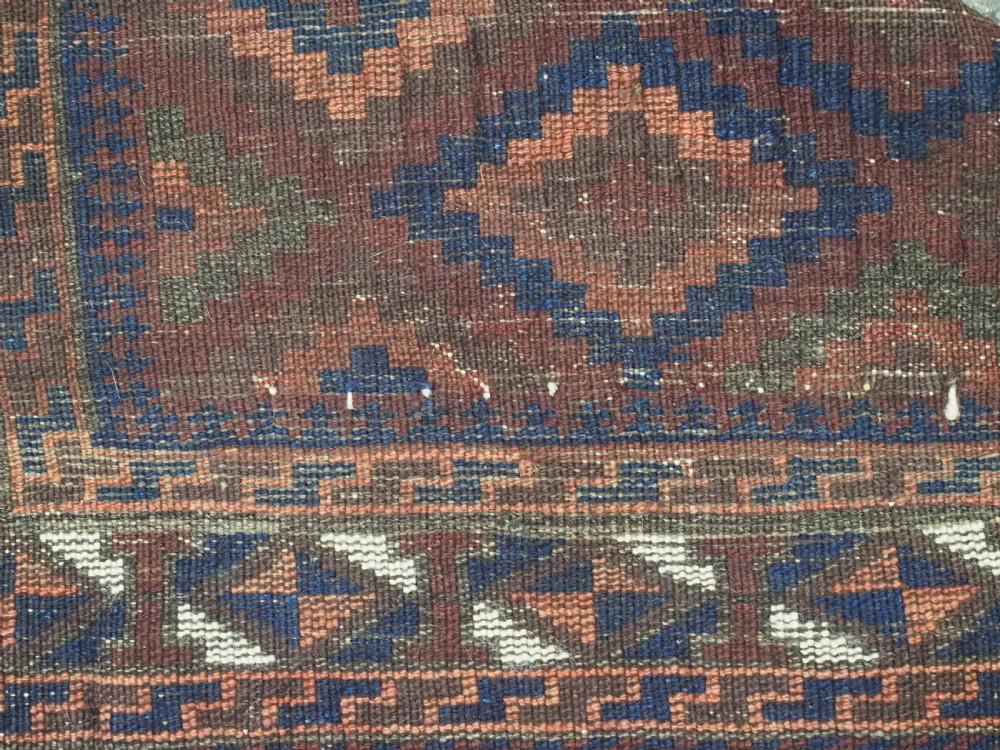An antique hand-knotted wool rug featuring a repeating diamond lattice pattern in terracotta red and dark navy blue with geometric borders and fringed edges. View IX