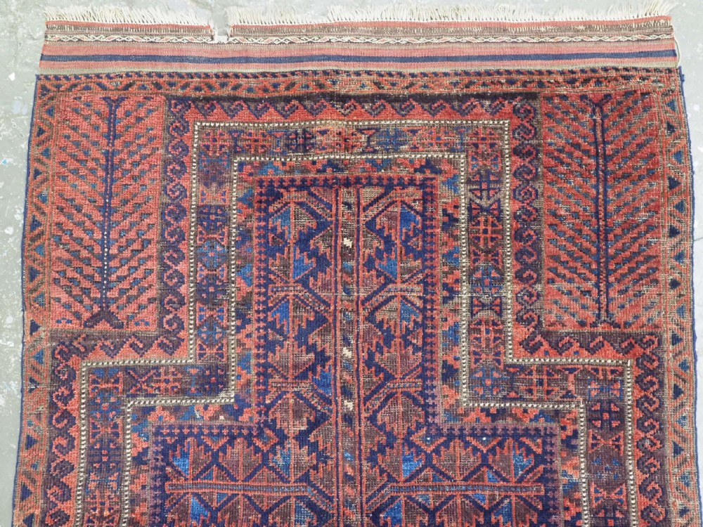 An antique hand-knotted Baluch prayer rug featuring a dark blue central field decorated with geometric motifs framed by a stepped arch and multi-tiered red borders. View III