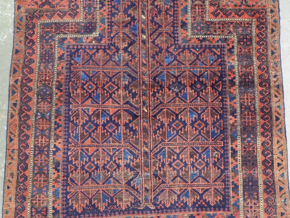 An antique hand-knotted Baluch prayer rug featuring a dark blue central field decorated with geometric motifs framed by a stepped arch and multi-tiered red borders. View IV