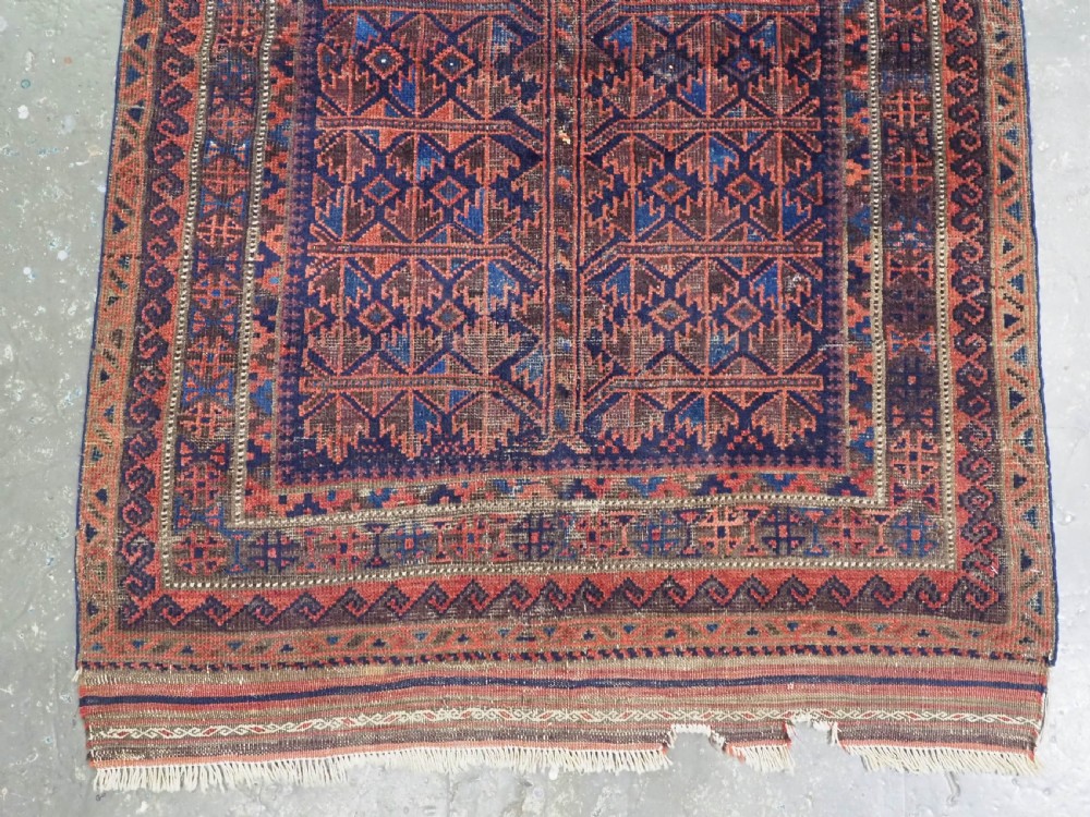 An antique hand-knotted Baluch prayer rug featuring a dark blue central field decorated with geometric motifs framed by a stepped arch and multi-tiered red borders. View V