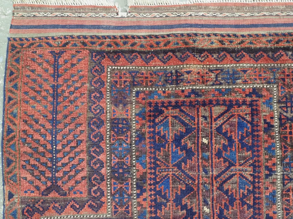 An antique hand-knotted Baluch prayer rug featuring a dark blue central field decorated with geometric motifs framed by a stepped arch and multi-tiered red borders. View VI