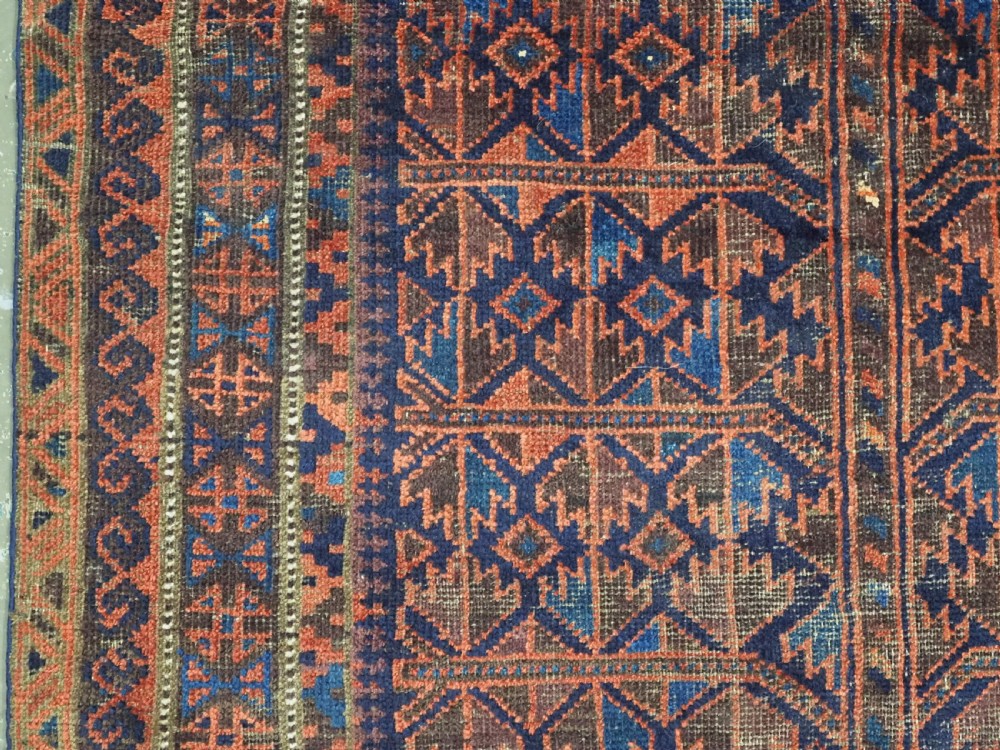 An antique hand-knotted Baluch prayer rug featuring a dark blue central field decorated with geometric motifs framed by a stepped arch and multi-tiered red borders. View VII
