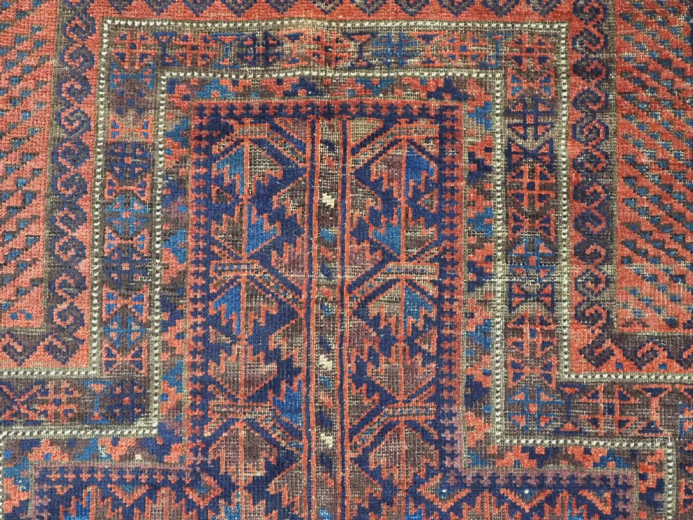An antique hand-knotted Baluch prayer rug featuring a dark blue central field decorated with geometric motifs framed by a stepped arch and multi-tiered red borders. View VIII