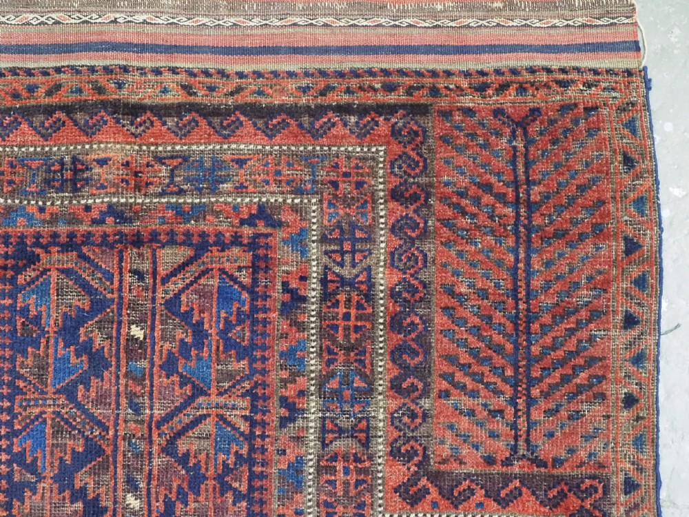 An antique hand-knotted Baluch prayer rug featuring a dark blue central field decorated with geometric motifs framed by a stepped arch and multi-tiered red borders. View IX
