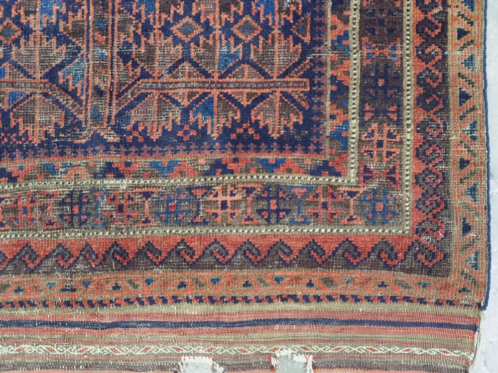 An antique hand-knotted Baluch prayer rug featuring a dark blue central field decorated with geometric motifs framed by a stepped arch and multi-tiered red borders. View XII