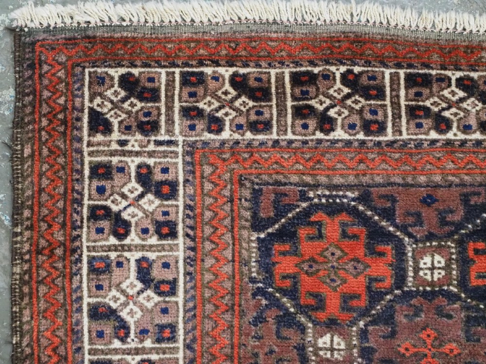 An antique rectangular Baluch wool rug featuring a dark central field with repeating geometric lattice patterns and a light ivory patterned border. View VI