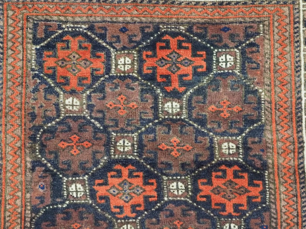 An antique rectangular Baluch wool rug featuring a dark central field with repeating geometric lattice patterns and a light ivory patterned border. View VIII