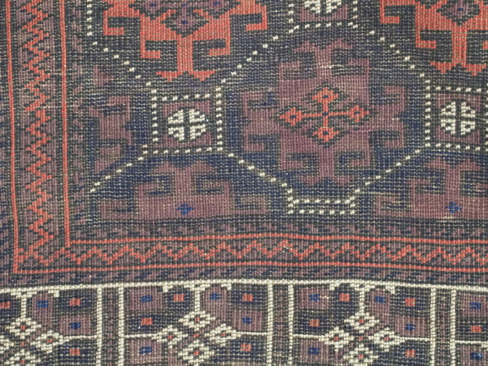 An antique rectangular Baluch wool rug featuring a dark central field with repeating geometric lattice patterns and a light ivory patterned border. View XI