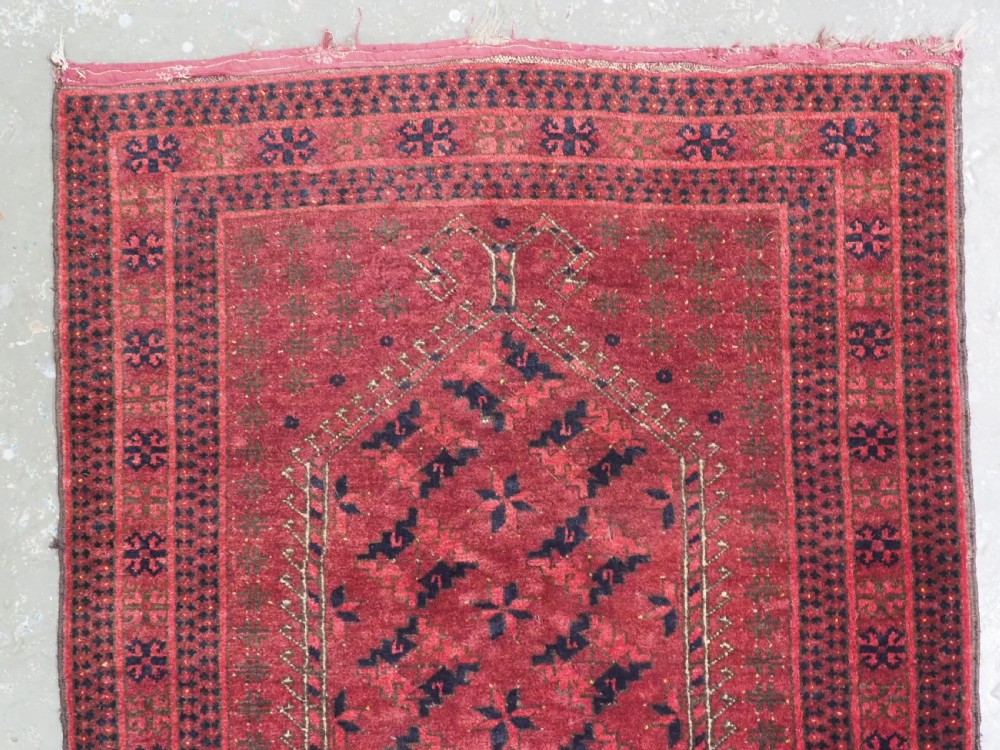 An antique red hand-knotted Turkmen wool prayer rug featuring an arched mihrab motif flanked by geometric rams horn symbols and multi-band borders. View III