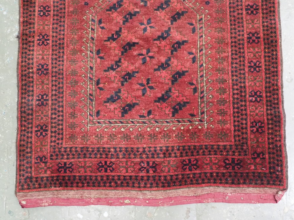 An antique red hand-knotted Turkmen wool prayer rug featuring an arched mihrab motif flanked by geometric rams horn symbols and multi-band borders. View IV