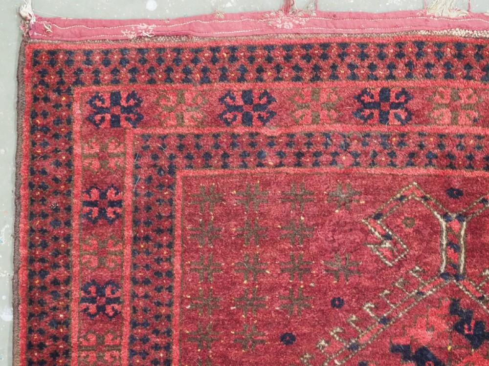 An antique red hand-knotted Turkmen wool prayer rug featuring an arched mihrab motif flanked by geometric rams horn symbols and multi-band borders. View V
