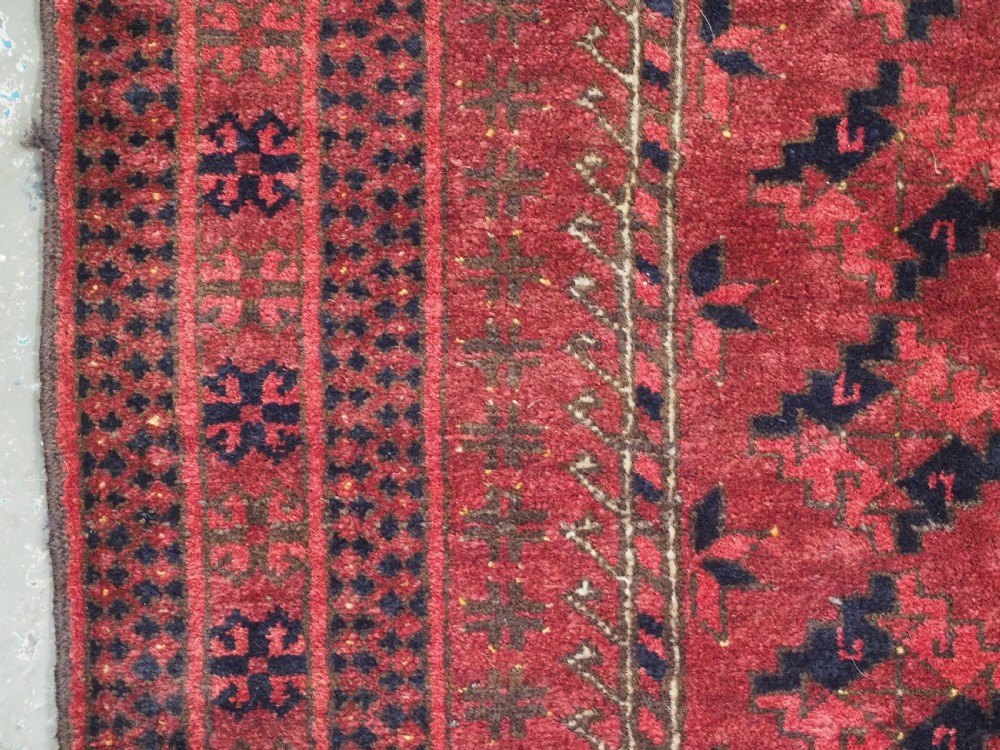 An antique red hand-knotted Turkmen wool prayer rug featuring an arched mihrab motif flanked by geometric rams horn symbols and multi-band borders. View VI