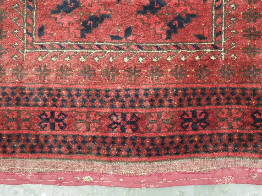 An antique red hand-knotted Turkmen wool prayer rug featuring an arched mihrab motif flanked by geometric rams horn symbols and multi-band borders. View VII