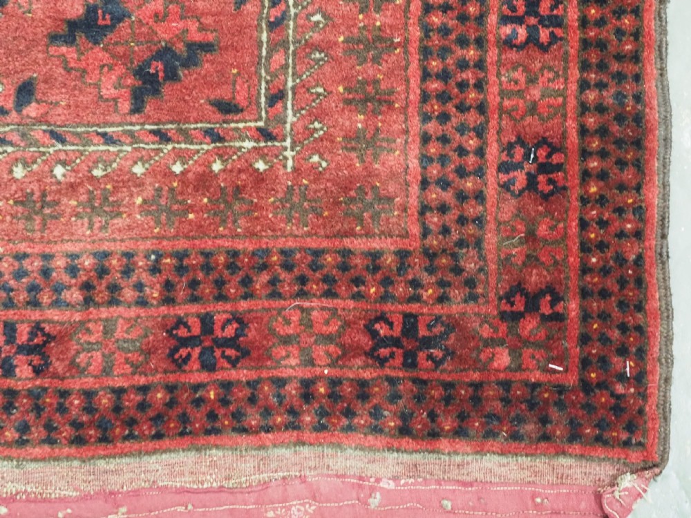 An antique red hand-knotted Turkmen wool prayer rug featuring an arched mihrab motif flanked by geometric rams horn symbols and multi-band borders. View VIII