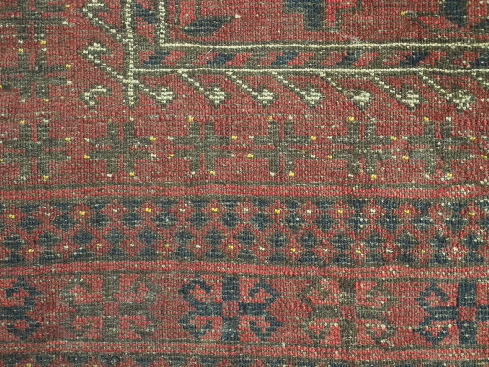 An antique red hand-knotted Turkmen wool prayer rug featuring an arched mihrab motif flanked by geometric rams horn symbols and multi-band borders. View IX
