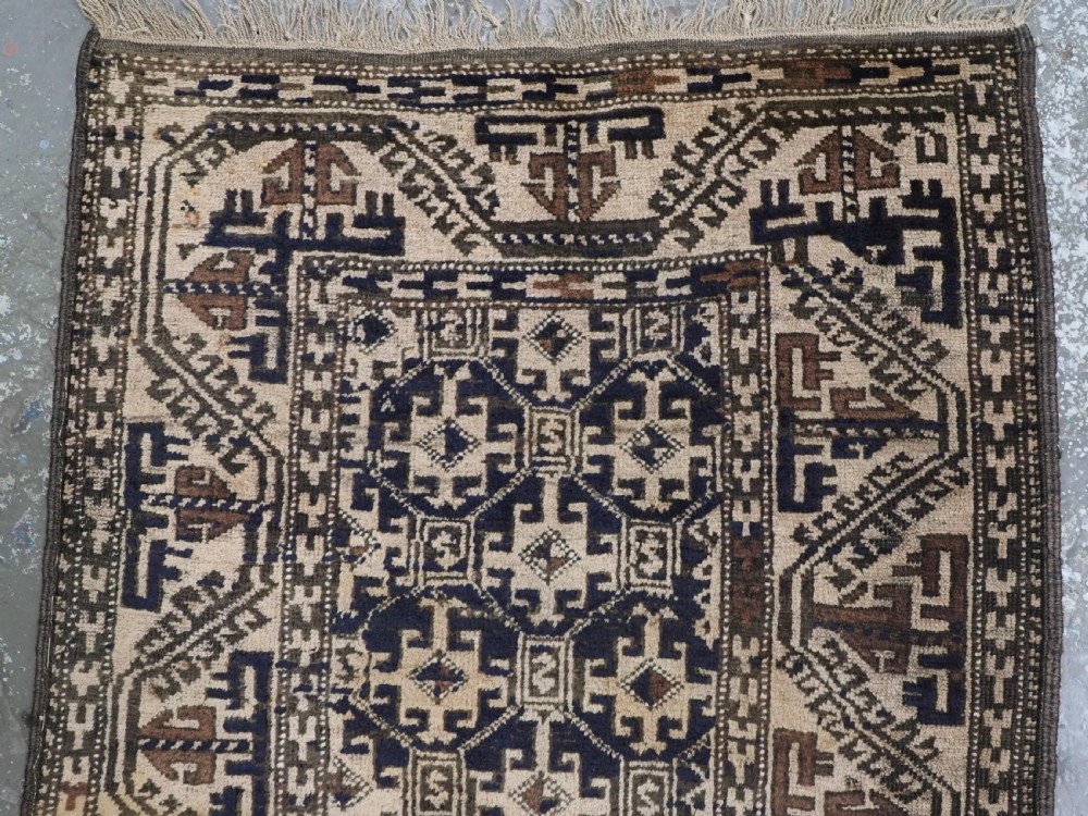 An antique woven Baluch rug featuring intricate geometric medallion patterns in shades of beige, brown, and dark indigo camel wool. View III