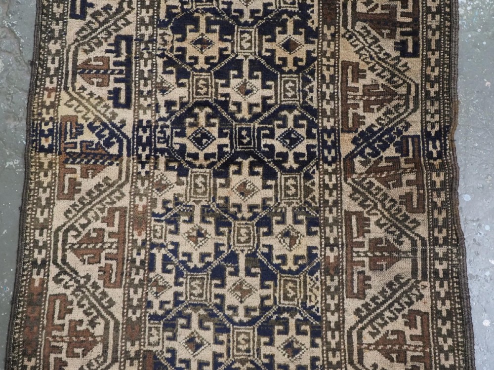 An antique woven Baluch rug featuring intricate geometric medallion patterns in shades of beige, brown, and dark indigo camel wool. View IV
