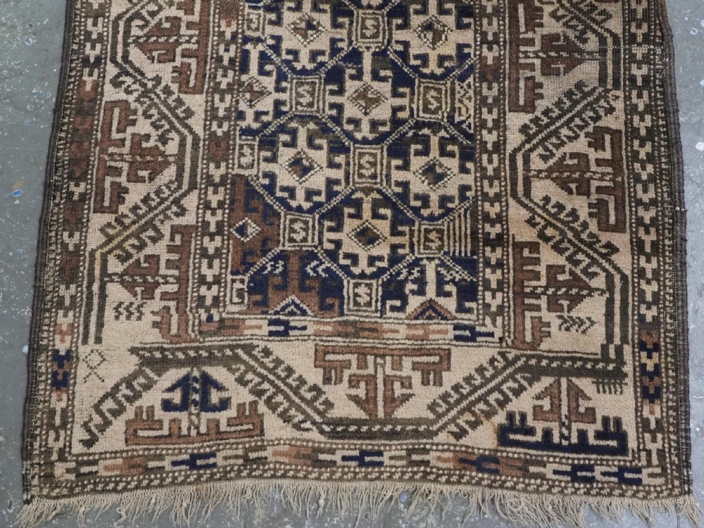 An antique woven Baluch rug featuring intricate geometric medallion patterns in shades of beige, brown, and dark indigo camel wool. View V
