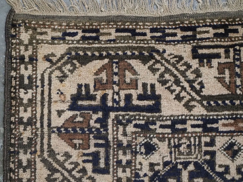 An antique woven Baluch rug featuring intricate geometric medallion patterns in shades of beige, brown, and dark indigo camel wool. View VI