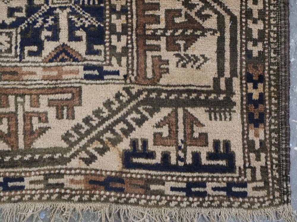 An antique woven Baluch rug featuring intricate geometric medallion patterns in shades of beige, brown, and dark indigo camel wool. View VII