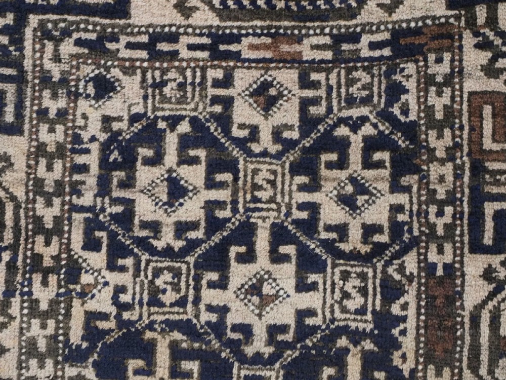 An antique woven Baluch rug featuring intricate geometric medallion patterns in shades of beige, brown, and dark indigo camel wool. View VIII