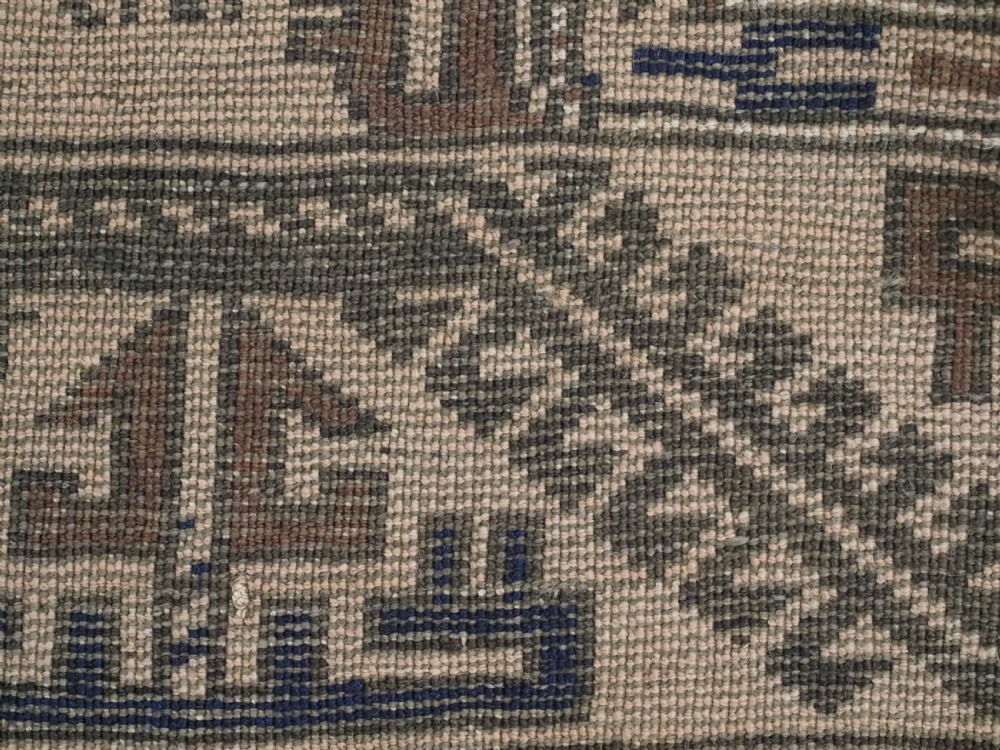 An antique woven Baluch rug featuring intricate geometric medallion patterns in shades of beige, brown, and dark indigo camel wool. View IX